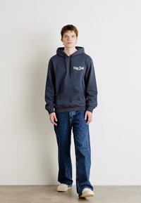 Mørkeblå hettegenser med "New York" grafikk, parret med vide blå jeans og lyse sneakers. Enkelt design og avslappet passform.