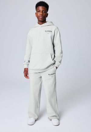 Teenage boy wearing a light gray AllSaints hoodie and matching sweatpants with white sneakers, standing against a plain background.