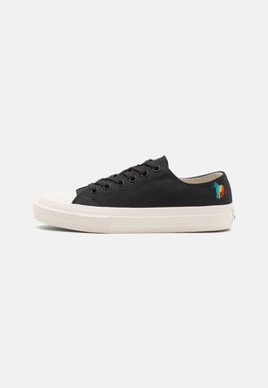 Zapatilla deportiva negra de lona de caña baja con suela y puntera de goma blanca, con logo de caballo multicolor bordado en el talón.