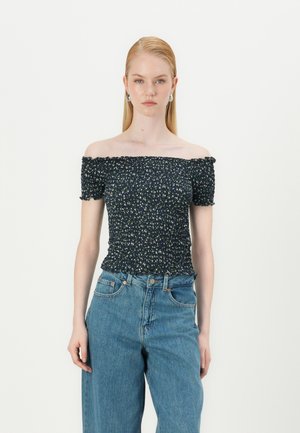 Haut navy à épaules dénudées avec imprimé floral, texture smockée et bords froncés ; associé à un jean taille haute bleu clair.