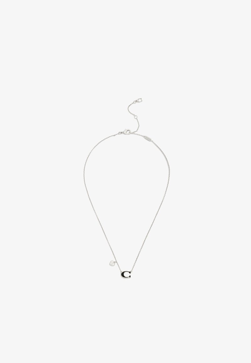 Collier chaîne en argent avec un pendentif "C" noir et argent et un petit charme en forme de cœur près du fermoir sur fond blanc.