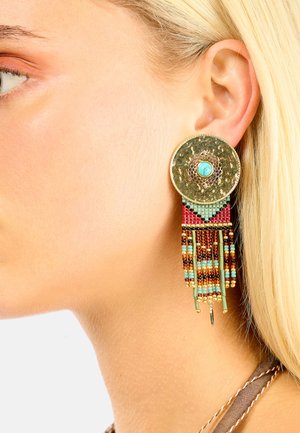 Boucles d'oreilles dorées avec un grand disque circulaire ornée d'une pierre turquoise, rehaussées d'une frange de perles colorées et de motifs complexes.