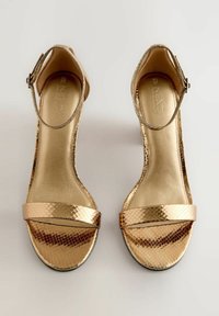 Auksinės basutės su tekstūruotu gyvatės odos raštu, su čiurnos dirželiu ir plačiomis priekinėmis juostomis. Lygus vidinis pamušalas ir plokščias padas.