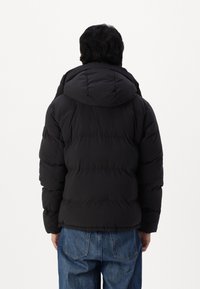 Svart puffjacka med huva, med ett quiltat mönster och ribbade ärmslut, i kombination med blå denimjeans för en lager på lager-look.
