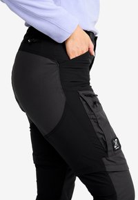 Svarta utomhusbyxor med en blandning av matt och strukturerad tyg, knädetaljer, fickor med dragkedja och en logotyp-patch på låret.