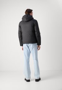 Svart polstret jakke med hette, med lange ermer og glatt tekstur, sammen med lyseblå denimjeans og svart fottøy.