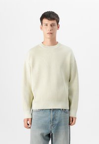 Pulover ribbed galben deschis, cu guler rotund și umeri lăsați, asortat cu blugi albastri decolorati. Textură netedă și croială lejeră.