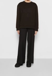 Schwarzer Sweatshirt mit "MARGIELA 6" in einer dunkleren Farbe auf der Vorderseite bedruckt, kombiniert mit locker sitzenden schwarzen Hosen und schwarzen Schuhen.