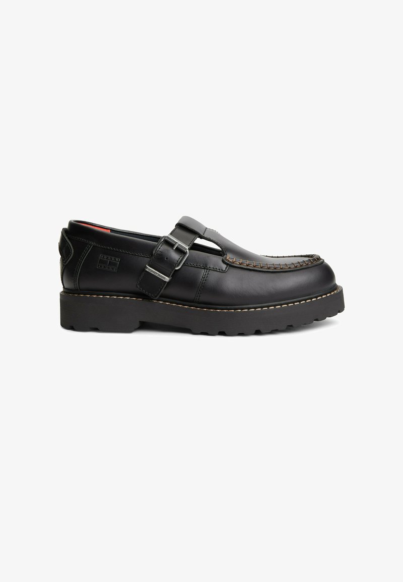 Black leather loafer with thick sole, side buckle strap, and contrast stitching on toe, shown in profile on white background.