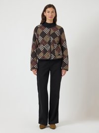 Woman standing wearing a brown, black, and cream checkered button-up jacket, black pants, and brown pointed shoes on a plain background.