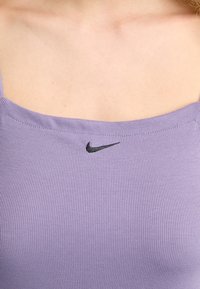 Top de tirantes de canalé púrpura con escote cuadrado y tirantes finos. Presenta un pequeño logo negro de Nike en el centro. Tejido suave y texturizado.