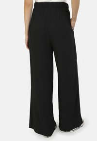 Pantaloni neri a gamba larga con una cintura elasticizzata, dotati di tasche laterali e di un tessuto leggero e liscio. Senza motivi visibili né accessori.