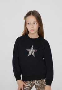 Černá mikina se vzorem leopardí hvězdy, s kulatým výstřihem a žebrovanými manžetami. Nošena s leopardími legínami.