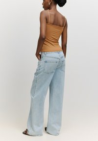 Hellblaue weit geschnittene Jeans mit hoher Taille und Vordertaschen, kombiniert mit einem enganliegenden, gerippten braunen Tanktop mit dünnen Trägern.
