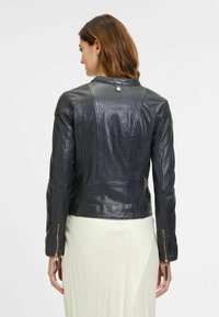 Zwarte leren jas met een slim fit ontwerp, voorzien van een ritssluiting en gouden accenten. Textuur op de schouders en naaddetails.