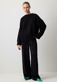 Black knitted sweater with a loose fit and ribbed cuffs paired with black patterned wide-leg pants and green flat shoes.
