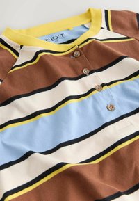 Top a maniche corte a righe nei colori marrone, blu, crema e giallo. Presenta una scollatura tonda, una patta con bottoni e una texture del tessuto morbida.