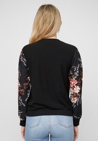 Schwarzer Sweatshirt mit blumig gemusterten Ärmeln, Rundhalsausschnitt und gerippten Bündchen, aus weichem Stoff mit legerem Schnitt.