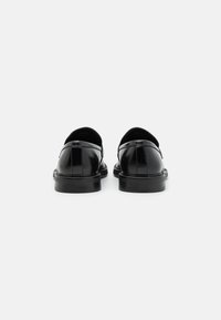 Zapatos de cuero negro con un acabado suave, punta redondeada y suela baja de goma negra. La vista trasera muestra costuras sutiles y un diseño minimalista.