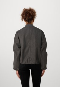 Jacket bomber cinza com colarinho canelado, mangas largas e bainha ajustada na parte inferior. Feita de tecido texturizado com um acabamento suave.