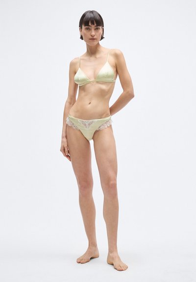 Világoszöld szatén melltartó vékony pántokkal és mély V-nyakkivágással; a hozzá illő alsónemű csipkés szegéllyel és alacsony derekú szabással rendelkezik.