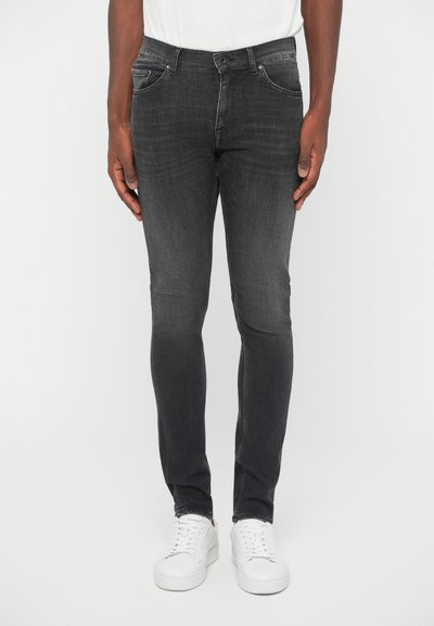 Σκούρες γκρίζες τζιν με slim fit, φτιαγμένες από τζιν. Διαθέτουν πέντε τσέπες και φερμουάρ. Φοριούνται με λευκά αθλητικά παπούτσια και λευκό T-shirt.