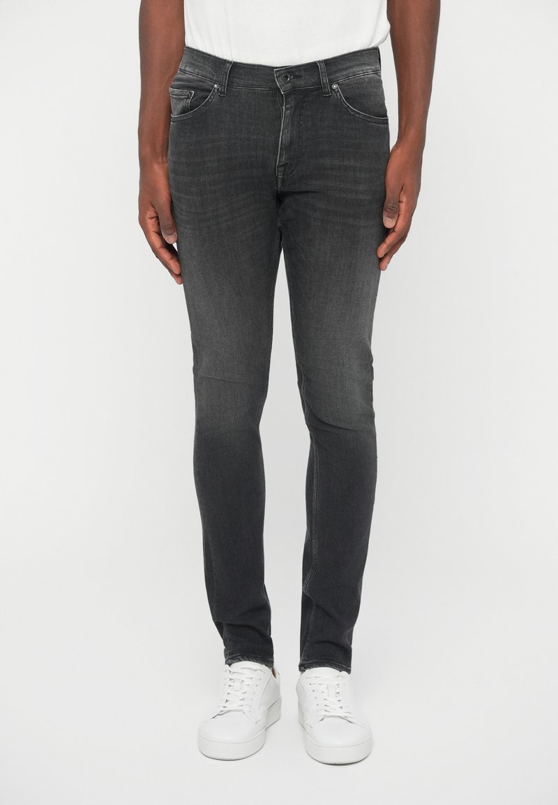 Blugi gri închis cu o potrivire slim, din denim. Au cinci buzunare și fermoar. Purtați cu adidași albi și un tricou alb.