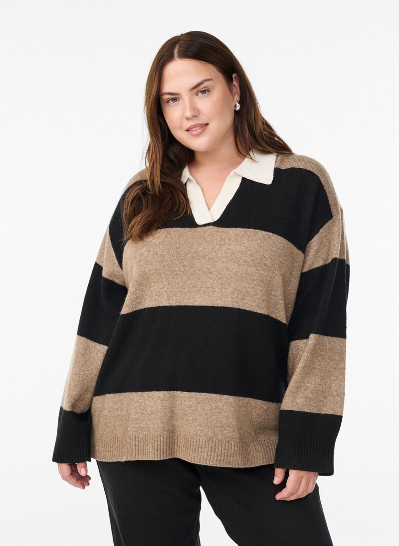 Kvinde med langt brunt hår iført en beige og sort bredstribet sweater over en hvid skjorte med krave mod en ensfarvet hvid baggrund.
