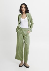 Light green two-piece outfit featuring a fitted blazer and wide-leg pants, made of soft, stretchy fabric, with front pleats and side pockets.