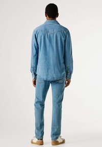 Světle modrá denimová košile a k ní ladící džíny s přiléhavým střihem. Má knoflíky na manžetách, špičatý límec a prošití na zadních kapsách.