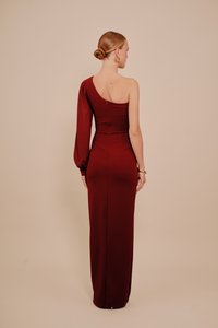 Bordowa wieczorowa suknia z jedną długą rękawem i dopasowaną sylwetką, z tylnym zamkiem i rozcięciem u dołu dla ułatwienia ruchu.