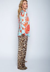 Lichtblauw top met bloemenpatroon en lange mouwen, gecombineerd met beige wijde broek met luipaardprint. Soepele texturen en contrasterende kleuren.