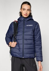 Marineblaue Steppjacke mit Reißverschluss und Kapuze. Verfügt über diagonale Nähte und ein gebrandetes Logo. Das Material sieht glatt und isoliert aus.