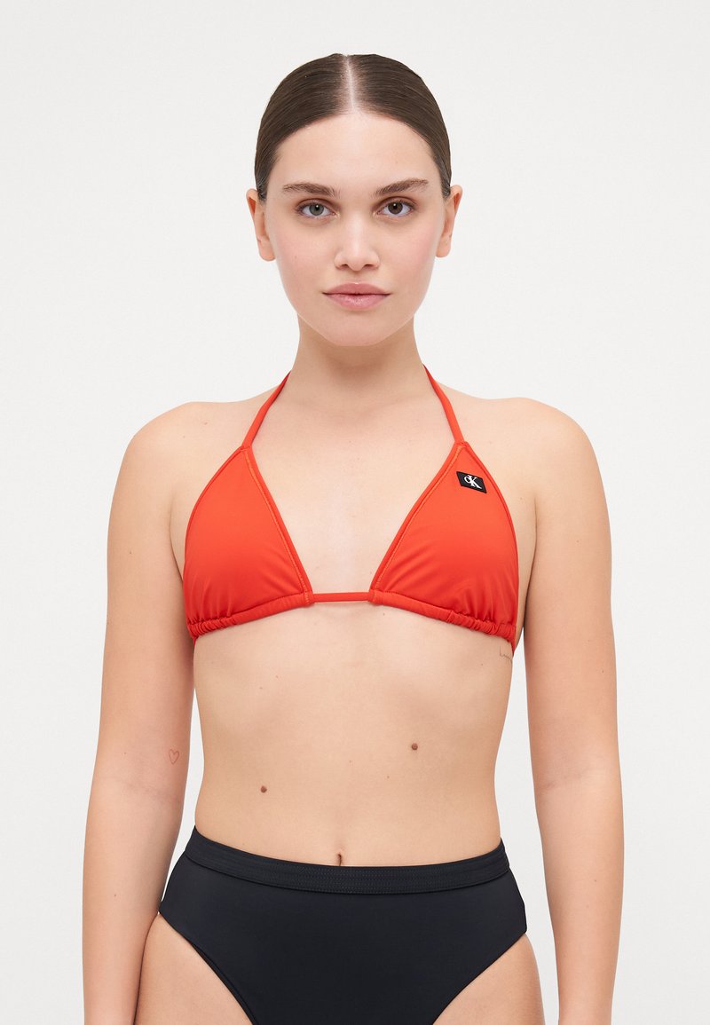 Röd bikiniöverdel med triangulära kupa och tunna band, med en logotypklack. Bärs med högmidjade svarta bikiniunderdelar.