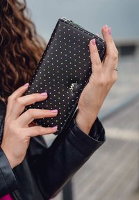 Black wallet with multicolored dot pattern, zip closure, and small logo detail. Held in hand, showcasing smooth leather texture.
