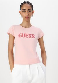 Rožinė medvilninė marškinė, ant kurių užrašyta "GUESS" drąsiu, šiek tiek nublukusiu šriftu. Trumpomis rankovėmis ir paprastu apvaliu iškarpymu.