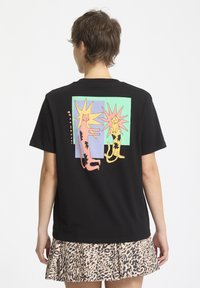 Camiseta de algodón negra con un gráfico divertido de dos gatos estilizados con destellos de colores sobre un fondo en menta y azul claro.