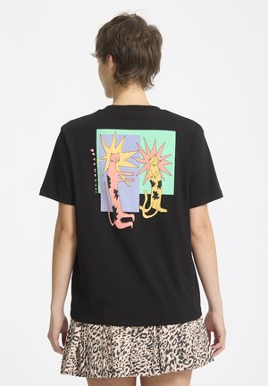 Camiseta de algodón negra con un gráfico divertido de dos gatos estilizados con destellos de colores sobre un fondo en menta y azul claro.