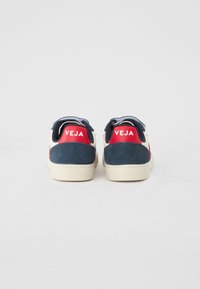 Bijele tenisice s akcentima od tamnoplave i crvene suede kože, s teksturiranim gornjim dijelom, mekanim ovratnikom i "VEJA" logotipom na peti.
