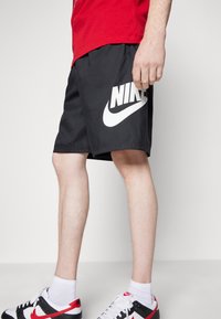 Black athletic shorts with a white "NIKE" logo on the left leg, paired with black and red sneakers, featuring white socks.
