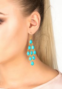 Pendientes de gota en tono dorado que presentan múltiples piedras en forma de lágrima de color turquesa con una superficie texturizada. Diseñados en un estilo en cascada.
