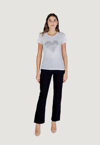 White short-sleeve t-shirt featuring a gray leopard print heart design, paired with black straight-leg pants and nude heels.