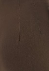 Primo piano di un tessuto marrone con due cuciture verticali e una fine texture, che mostra i dettagli delle cuciture su un materiale liscio.