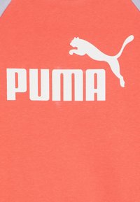 Koralowa bluzka z szarymi akcentami, z dużym białym logo "PUMA" i sylwetką skaczącego pumy. Wykonana z miękkiego bawełnianego materiału.