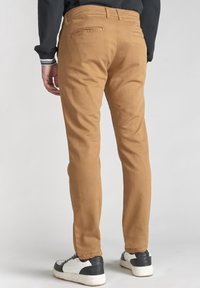 Avslappnade, slim-fit ljusbruna byxor i en bomullsblandning med bakfickor. Matchat med svarta och vita sneakers.