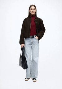 Svart bomberjakke, burgunder rullekragegenser, lyseblå vide bukser, svart belte, svart toteveske og svarte og hvite joggesko.