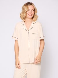 Lys beige pyjamasæt med korte ærmer, sort piping, en brystlomme og løstsiddende bukser i et blødt, struktureret stof.