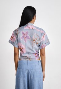 Camicia a manica corta con stampa floreale in azzurro chiaro, con motivi rosa e marroni. Presenta un colletto e le maniche arrotolate. Pantaloni corti in denim.