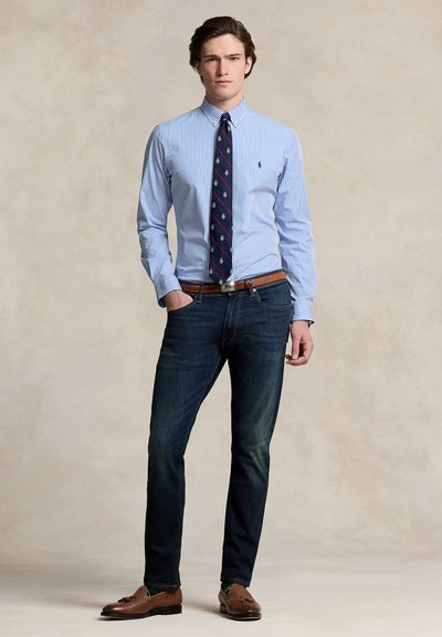 Košeľa na zapínanie s modrými a bielymi pruhmi, skombinovaná s tmavými džínsami. Hnedý opasok a mokasíny. Vzorovaná kravata s námorníckym podkladom a motívmi.