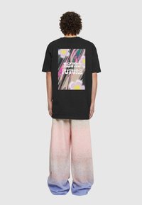 Melnā T-krekls ar krāsainu grafisku apdruku aizmugurē ar tekstu "RETRO NĀKOTNE." Apvienots ar vaļīgām, pasteļtoņu pārejas biksēm.